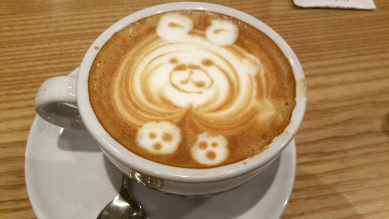 A cup of coffee with a teddy bear face in the crema